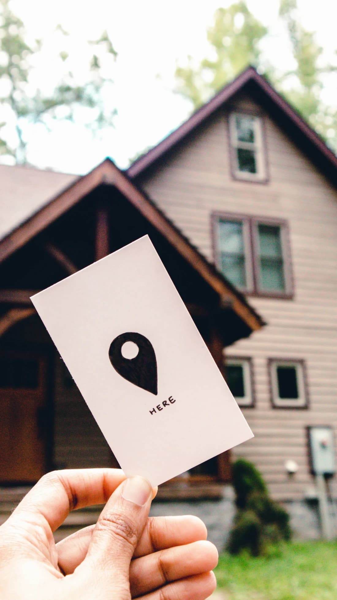 Hand holding a card marked "here" in front of a house