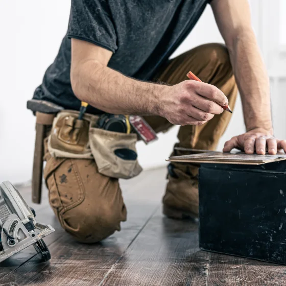 Handyman marking a floorboard next to a circular saw